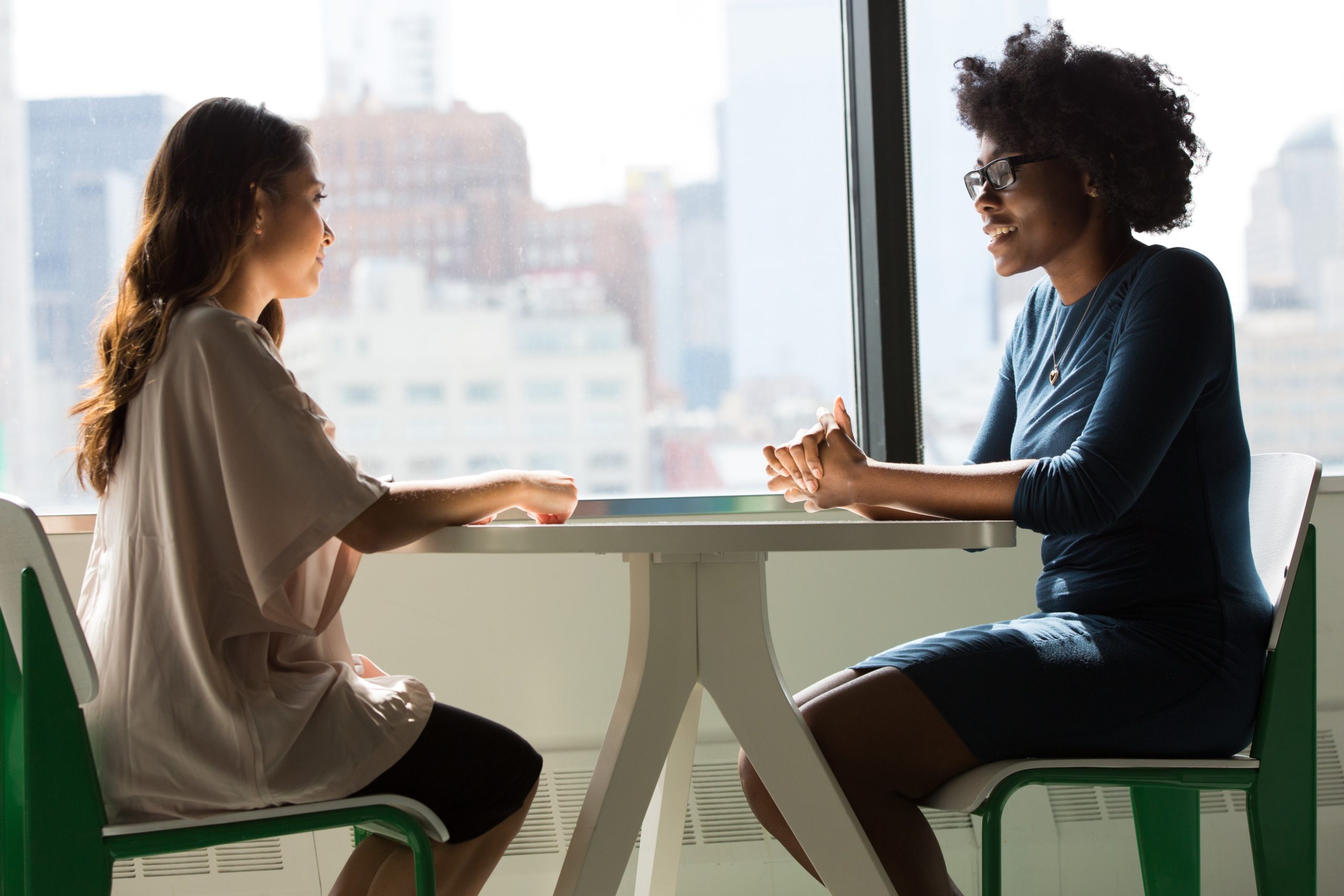 two-women-sitting-on-chairs-beside-window-11817192